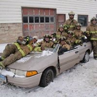group of firefighters posing on car
