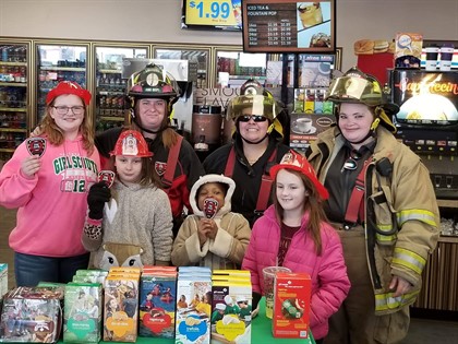 three firefighters and girl scouts in front of green table